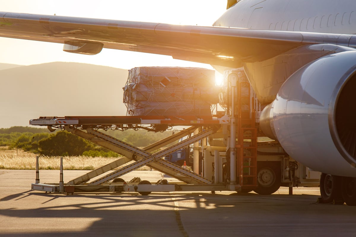 Workers loading cargo onto a commercial airplane at sunset